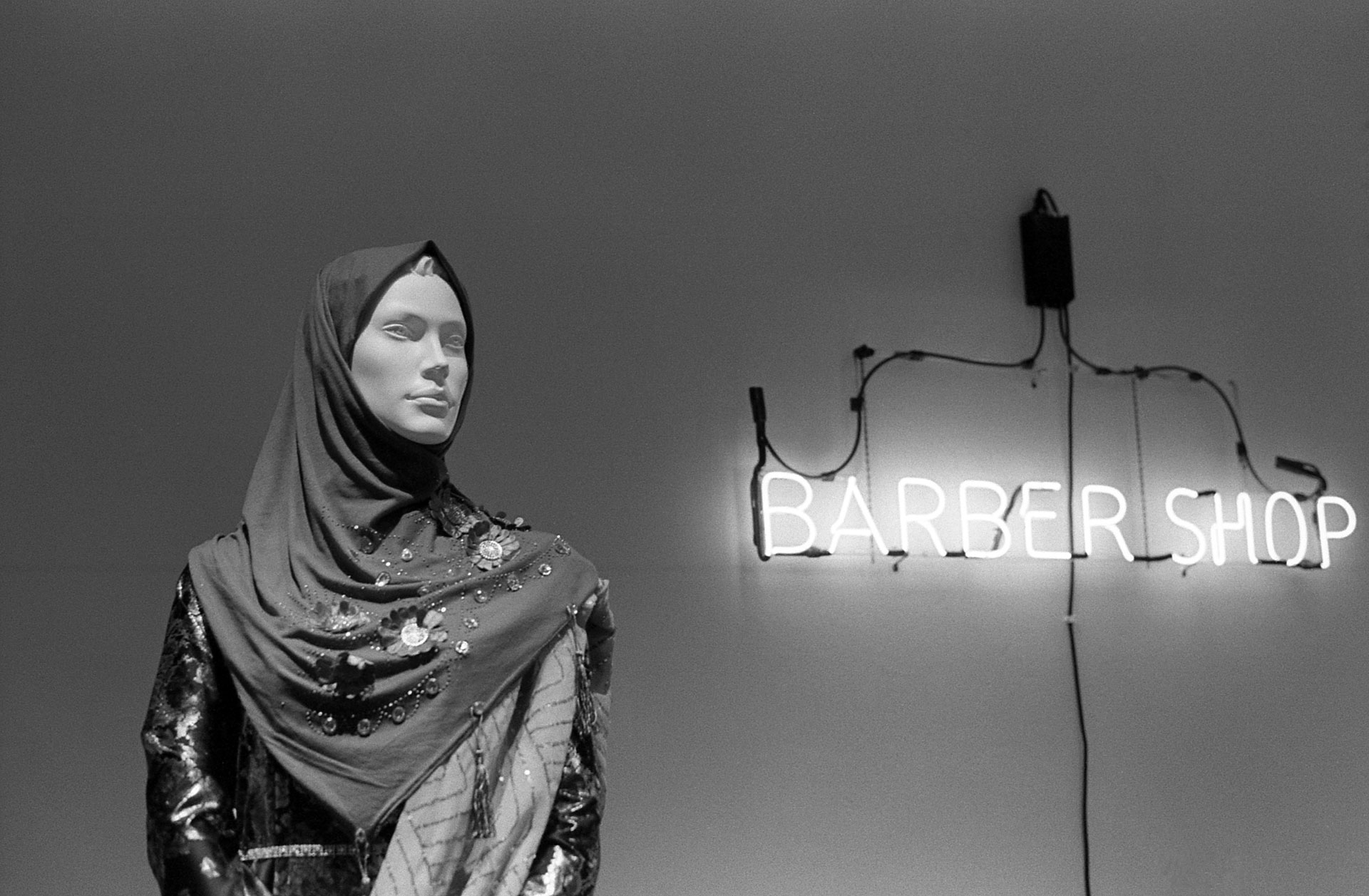 a mannequin which has the text barber shop behind it on a neon sign